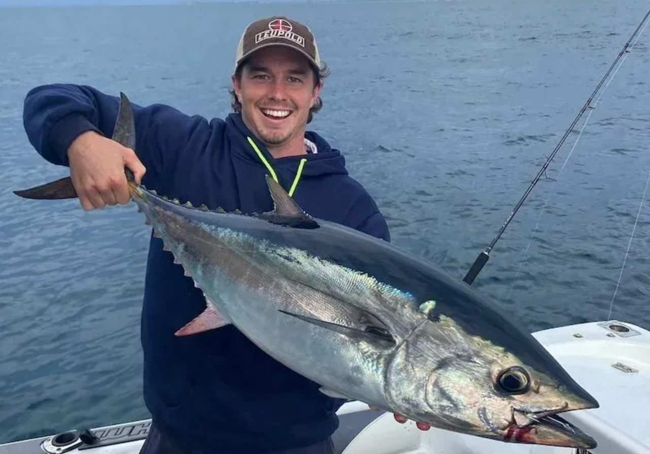 Adelaide Crows AFL footballer Ned McHenry smiling on a boat while holding up a large freshly caught bluefin tuna fish out at sea on a fishing trip.